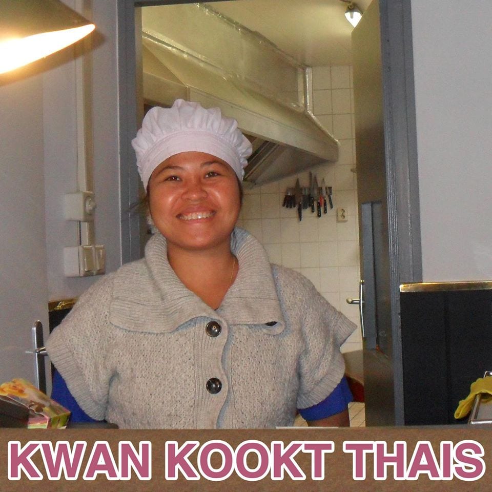 Kwan lachend in de keuken van Kwan kookt Thais, met het naambord van het restaurant